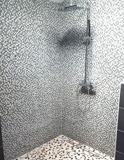 Création d'une douche à l'italienne avec parois en mosaïque grise, sol en galets et colonne de douche chromée, dans toute la vallée de l'Arve
